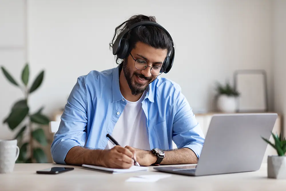 Happy Guy Wearing Headphones Studying Online With Laptop At Home