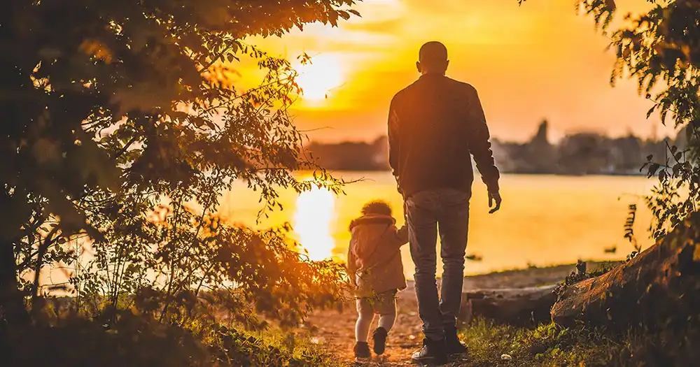 man with young toddler walking around a lake with the sun setting in the distance