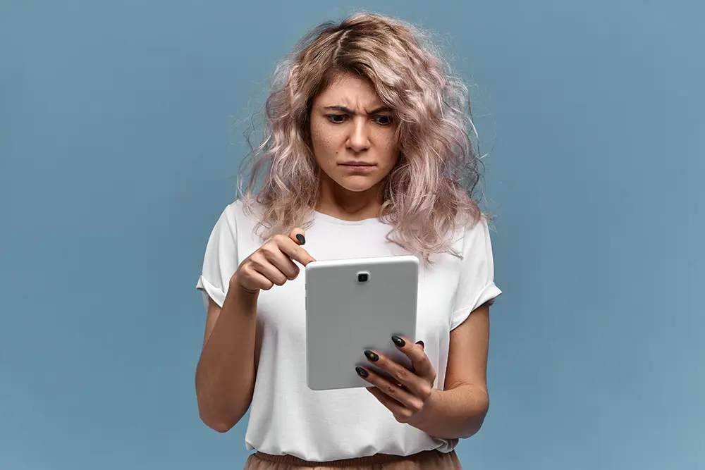 girl looks dismayed at a tablet in front of a blue background
